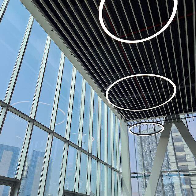 Kreisförmige, Ringo Star Pendelleuchten in unterschiedlichen Größen unter einer hohen Glasdecke mit schmalen, parallel verlaufenden Metallstreben.
