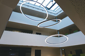 Three ring-shaped Ringo Star LED pendant lights from Lightnet in the light-flooded atrium of Delbrück Town Hall