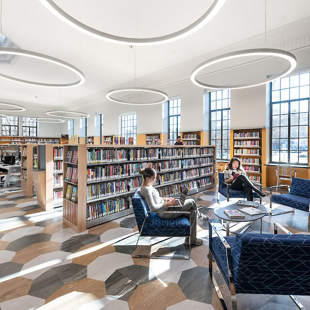 Bright library with Ringo Star pendant luminaires, bookshelves, reading area and geometric floor pattern.