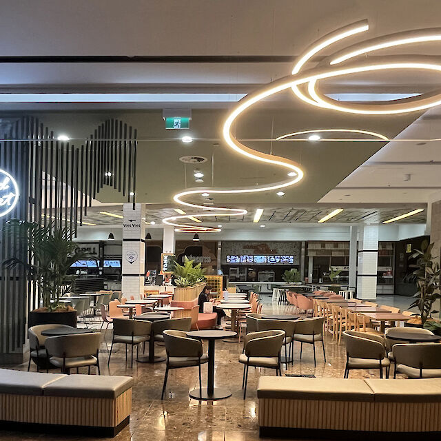 Modern food court with round seating islands and curved Liquid Line LED ceiling lights
