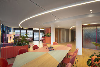 Large meeting area with colorful furniture, plants, and curved Liquid Line light lines on the ceiling.
