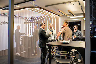 Several trade fair visitors chatting at the Lightnet booth, surrounded by chain curtains and modern lighting fixtures.