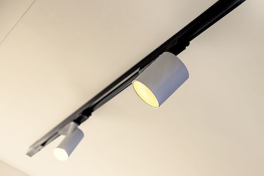 Two cylindrical LED spotlights in a black track, mounted against a light ceiling to provide warm lighting.