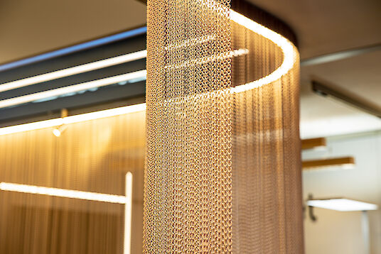 Gold-colored chain curtain with integrated light line creates warm, structured light effects in the room